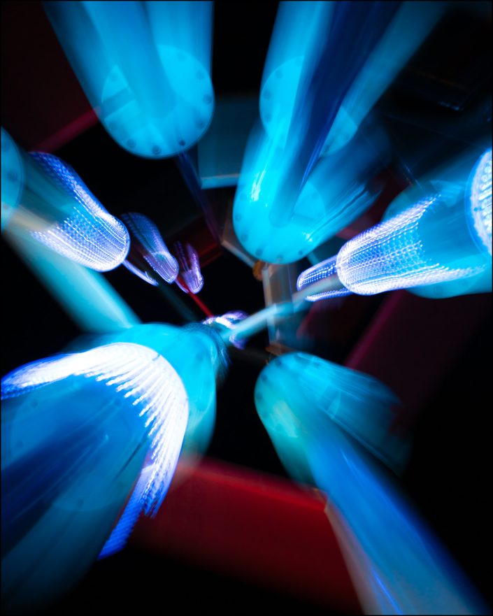 Features a water spray tower near the El Paso Convention Center, captured with slow shutter speed and zooming motion to create an electrifying burst of neon light, evoking the sensation of rapid acceleration or liftoff.