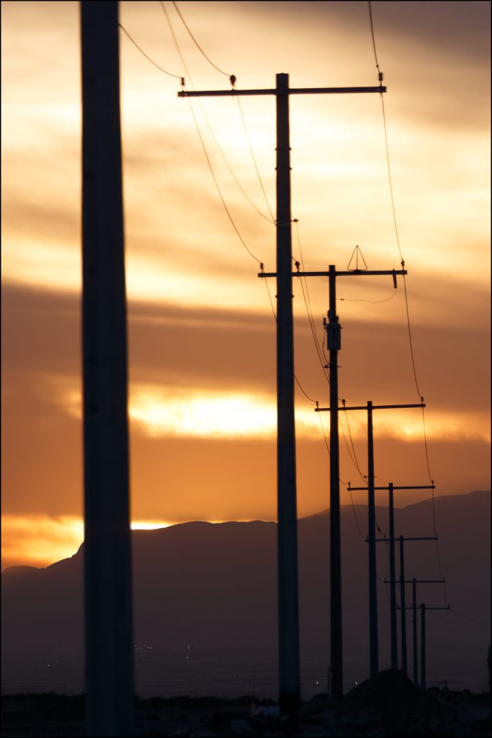 Sunset over the Mexican mountains seen from El Paso, Texas, with silhouetted peaks beneath a radiant sky, intersected by utility lines and poles, highlighting the contrast between nature's grandeur and human infrastructure.