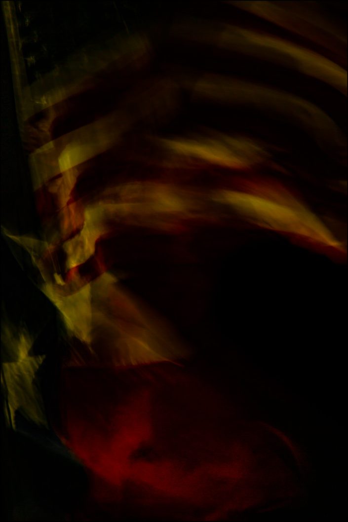 Features a painterly quality, abstract composition that creatively merges the American and Texas flags using slow shutter speed on a windy day to create fluid waves of color and light.