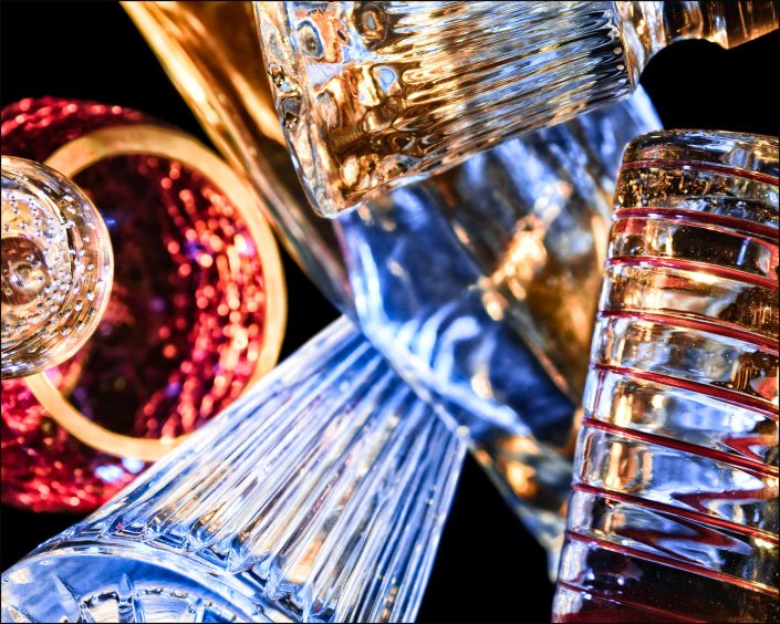 First abstract fine art photo from the ten-image series, "An Abyss of Glass & Color" which features vivid colors, highlights, and shadows on various layered glass objects. Captured from below, the image creates a sense of depth from the layered space by blending form, light, and color to evoke a vibrant, infinite void.