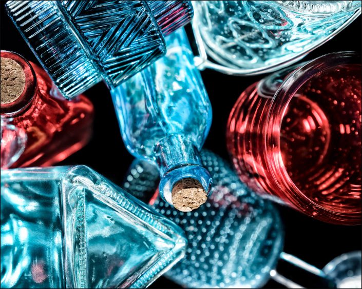 Third abstract fine art photo from the ten-image series, "An Abyss of Glass & Color" which features vivid colors, highlights, and shadows on various layered glass objects. Captured from below, the image creates a sense of depth from the layered space by blending form, light, and color to evoke a vibrant, infinite void.