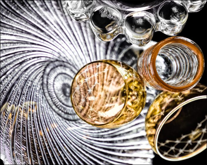 Fourth abstract fine art photo from the ten-image series, "An Abyss of Glass & Color" which features vivid colors, highlights, and shadows on various layered glass objects. Captured from below, the image creates a sense of depth from the layered space by blending form, light, and color to evoke a vibrant, infinite void.