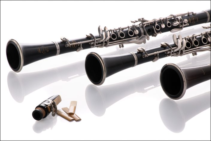 Three clarinets arranged symmetrically on a white background with soft reflections, highlighting classical music elegance, woodwind craftsmanship, and minimalist design.